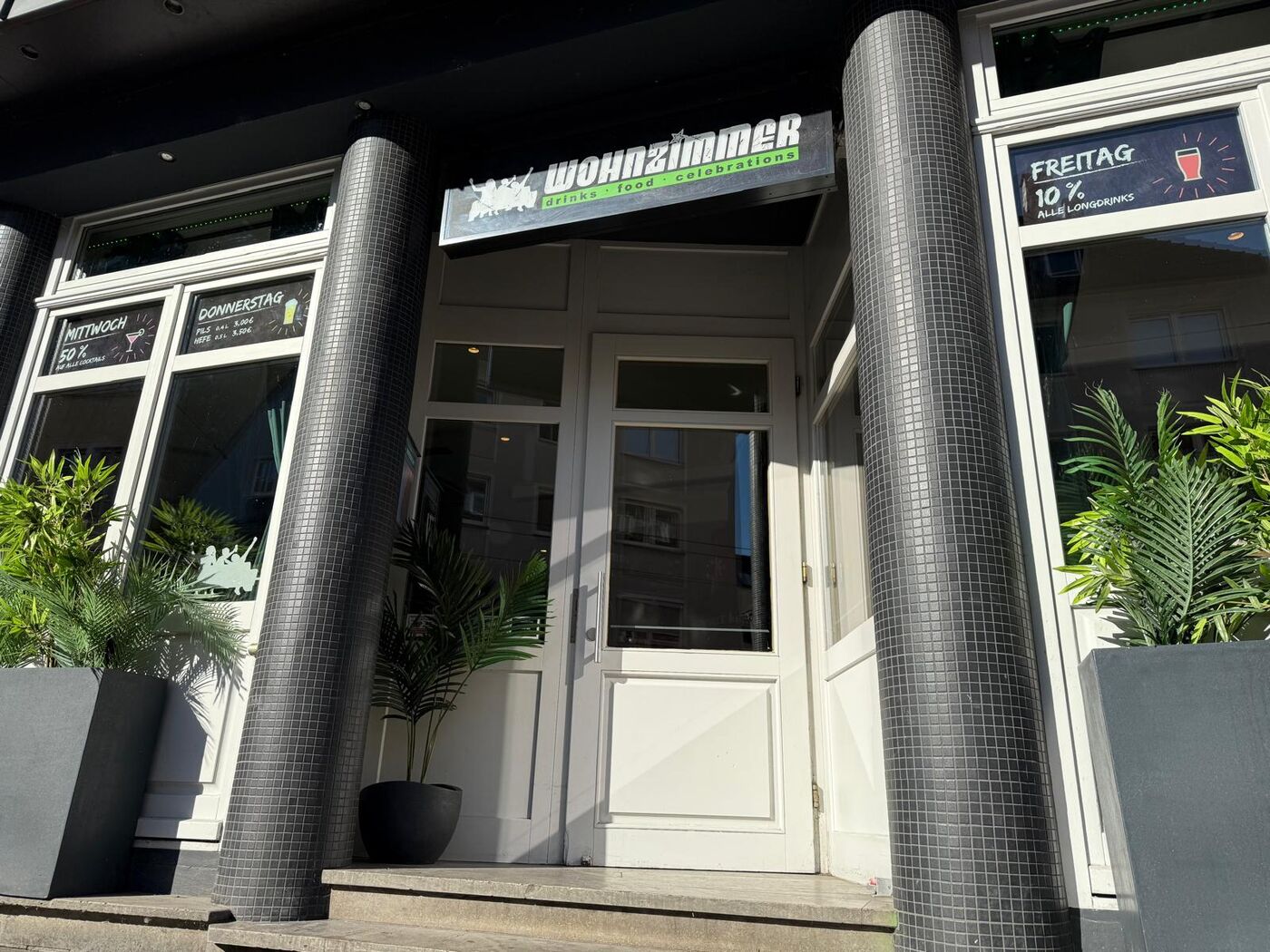 Eingang der Wohnzimmer Bar Würzburg mit Logo und Happy-Hour-Tafeln